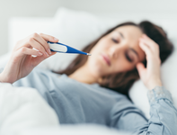 Frau liegt mit Fieber im Bett